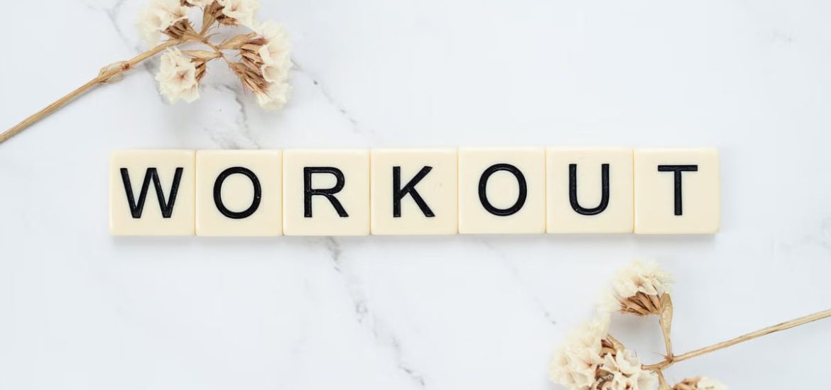 Letter tiles spelling 'WORKOUT' on marble with dried flowers, conveying fitness motivation.