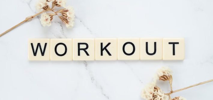 Letter tiles spelling 'WORKOUT' on marble with dried flowers, conveying fitness motivation.