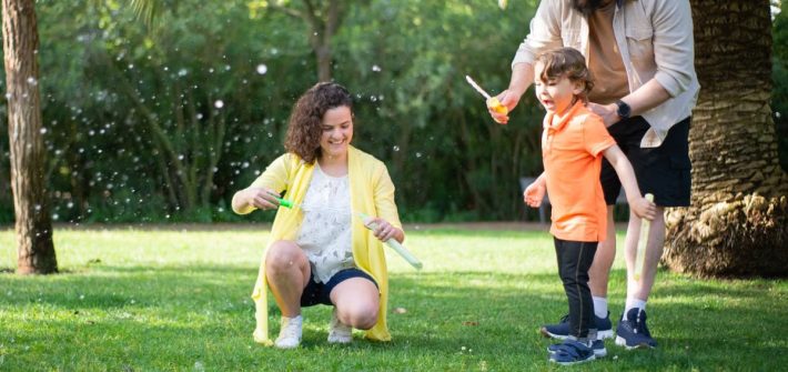 A family enjoys a playful day with bubbles in a sunny park setting.