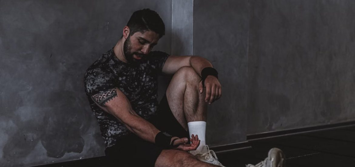 A muscular man in a gym environment taking a moment of rest, reflecting in a dark moody setting.